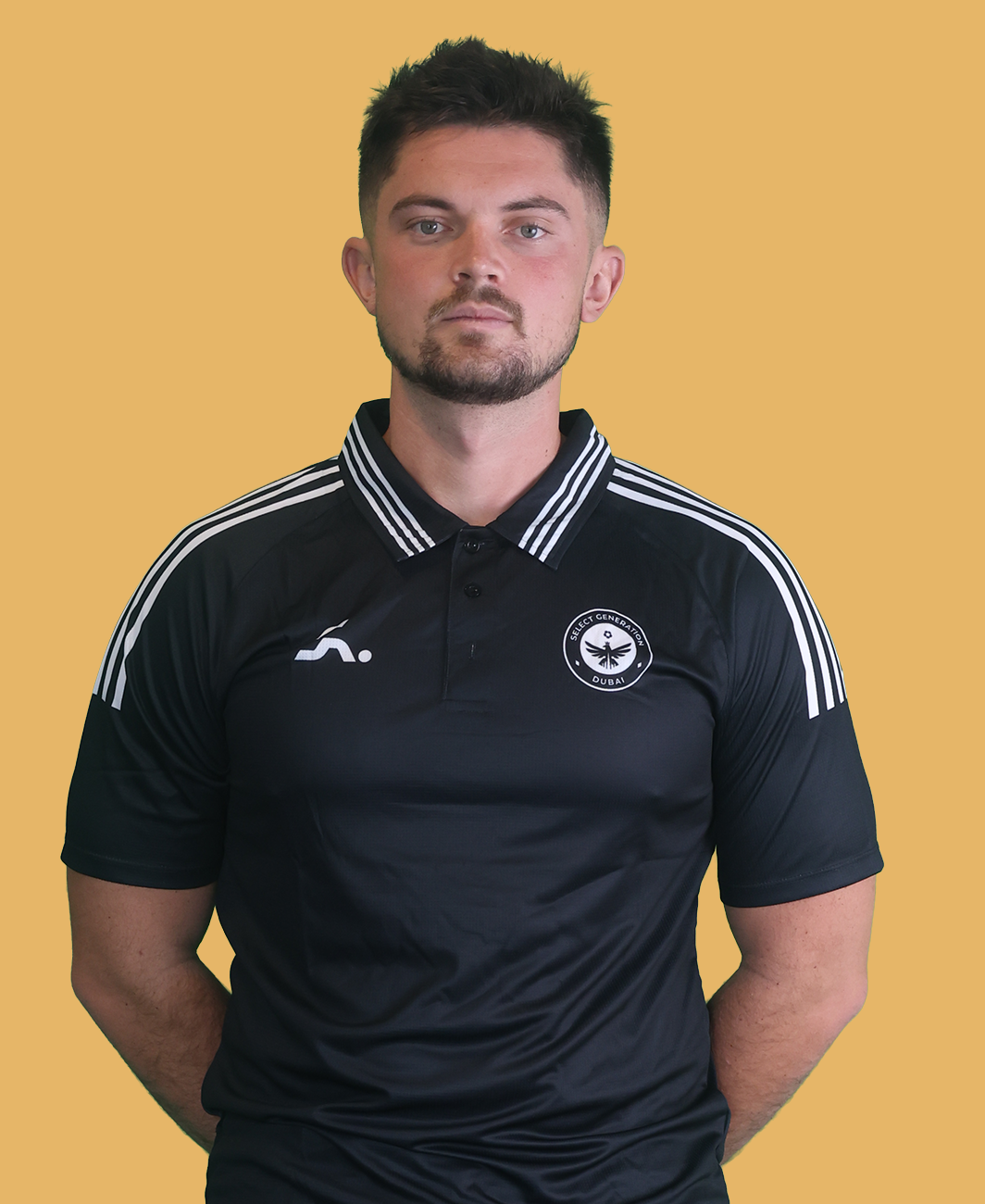Man with short dark hair and beard standing outdoors wearing a black sports shirt and pants.