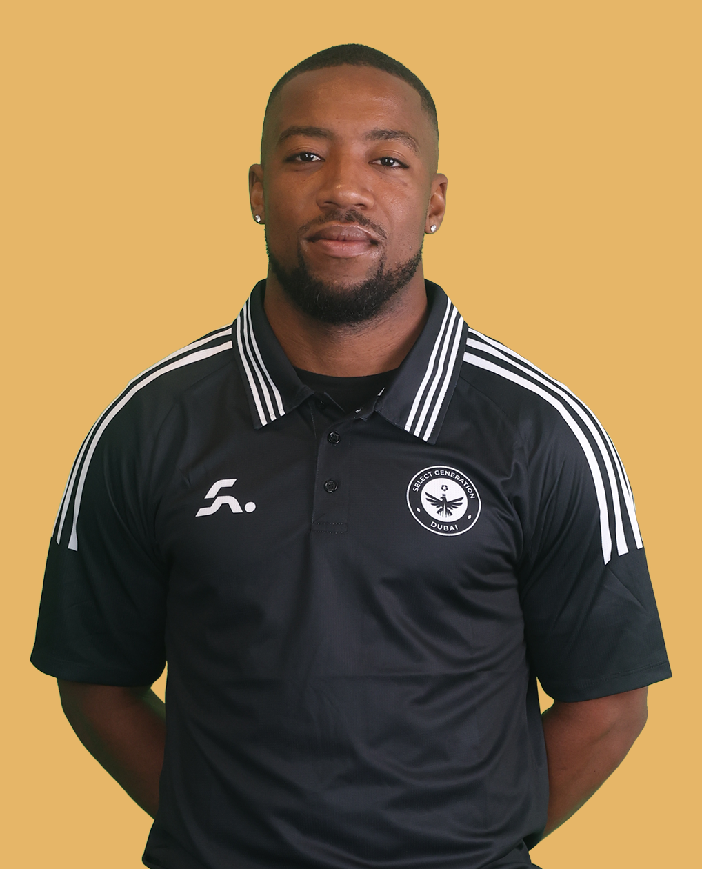 Man wearing a black polo shirt standing outdoors on a grassy field.