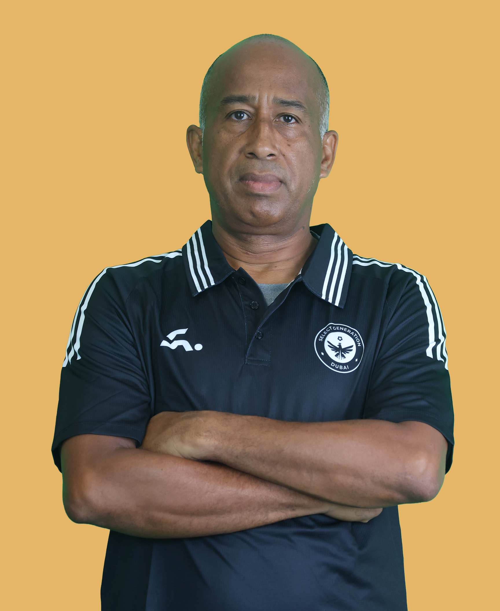 Man with arms crossed wearing a black Adidas t-shirt and a black cap against a plain light background.
