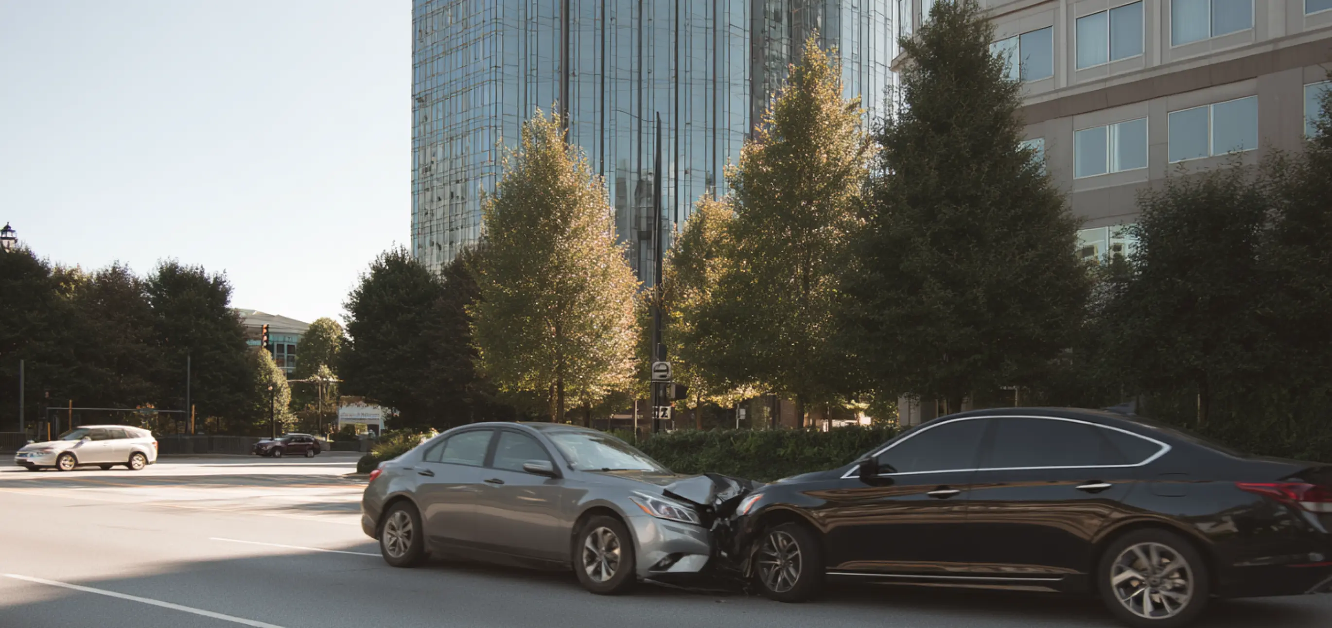 Two sedans with front-end damage involved in a head-on collision on a city street.