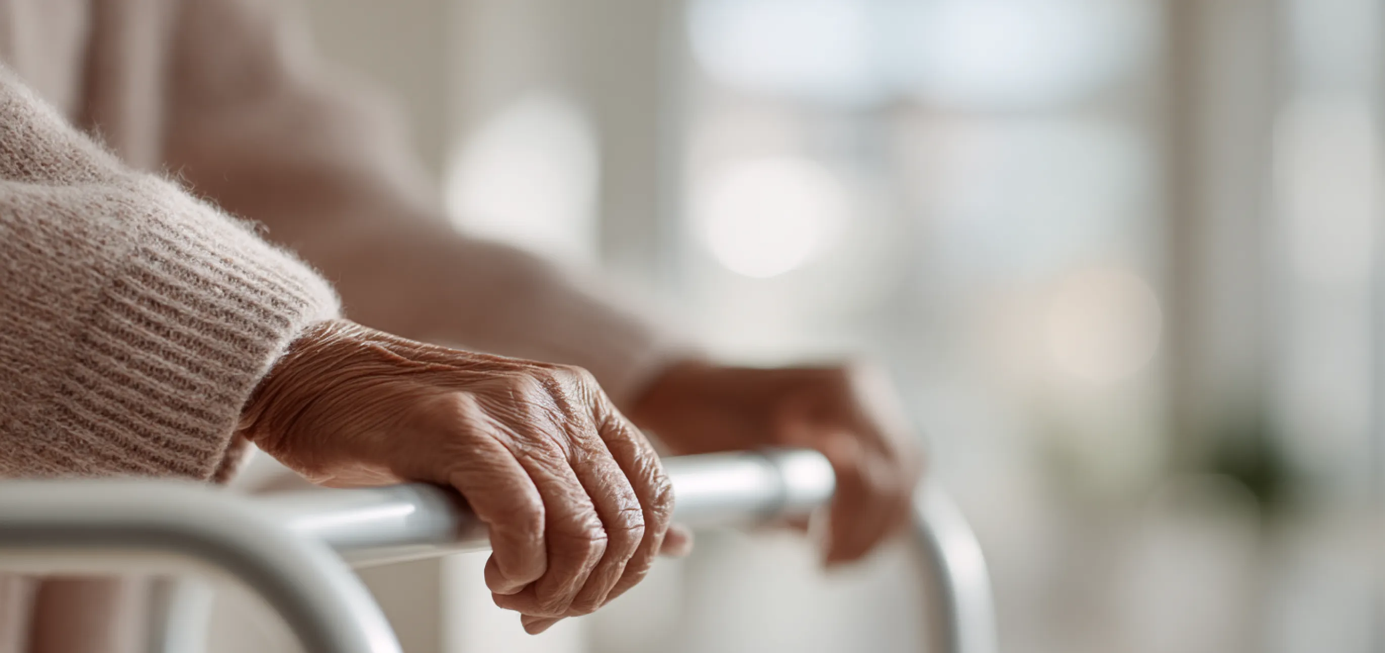 Close-up of an elderly person's hands gripping a metal walker indoors.