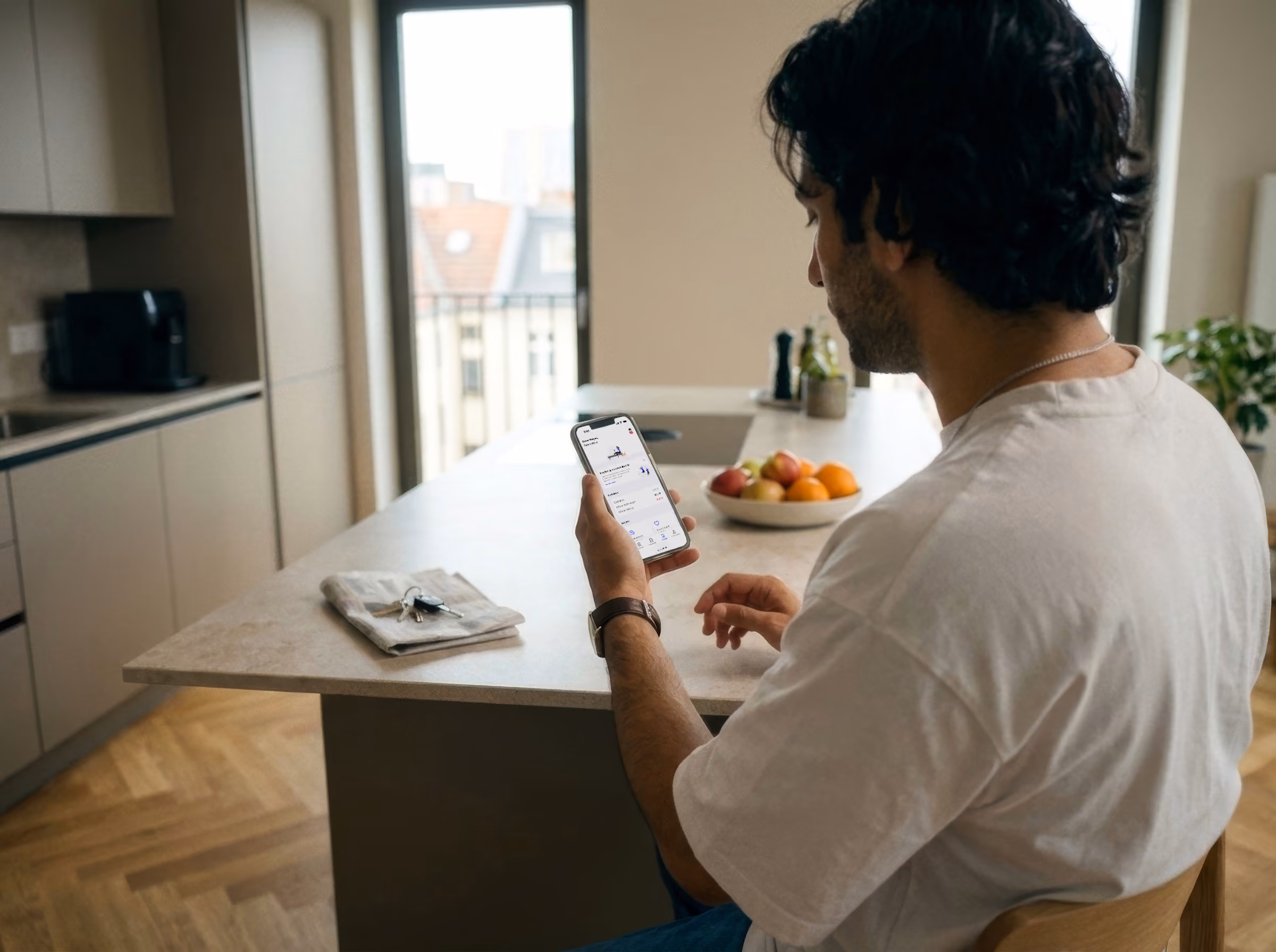 A man in a white T-shirt sits at a kitchen island looking at his phone.