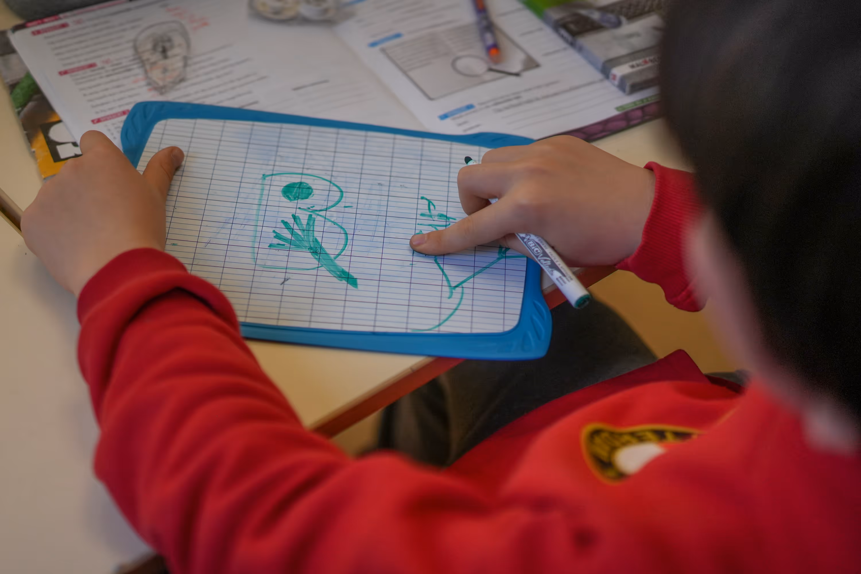 Kind tekent met groene marker op een klembord tijdens schoolactiviteiten.