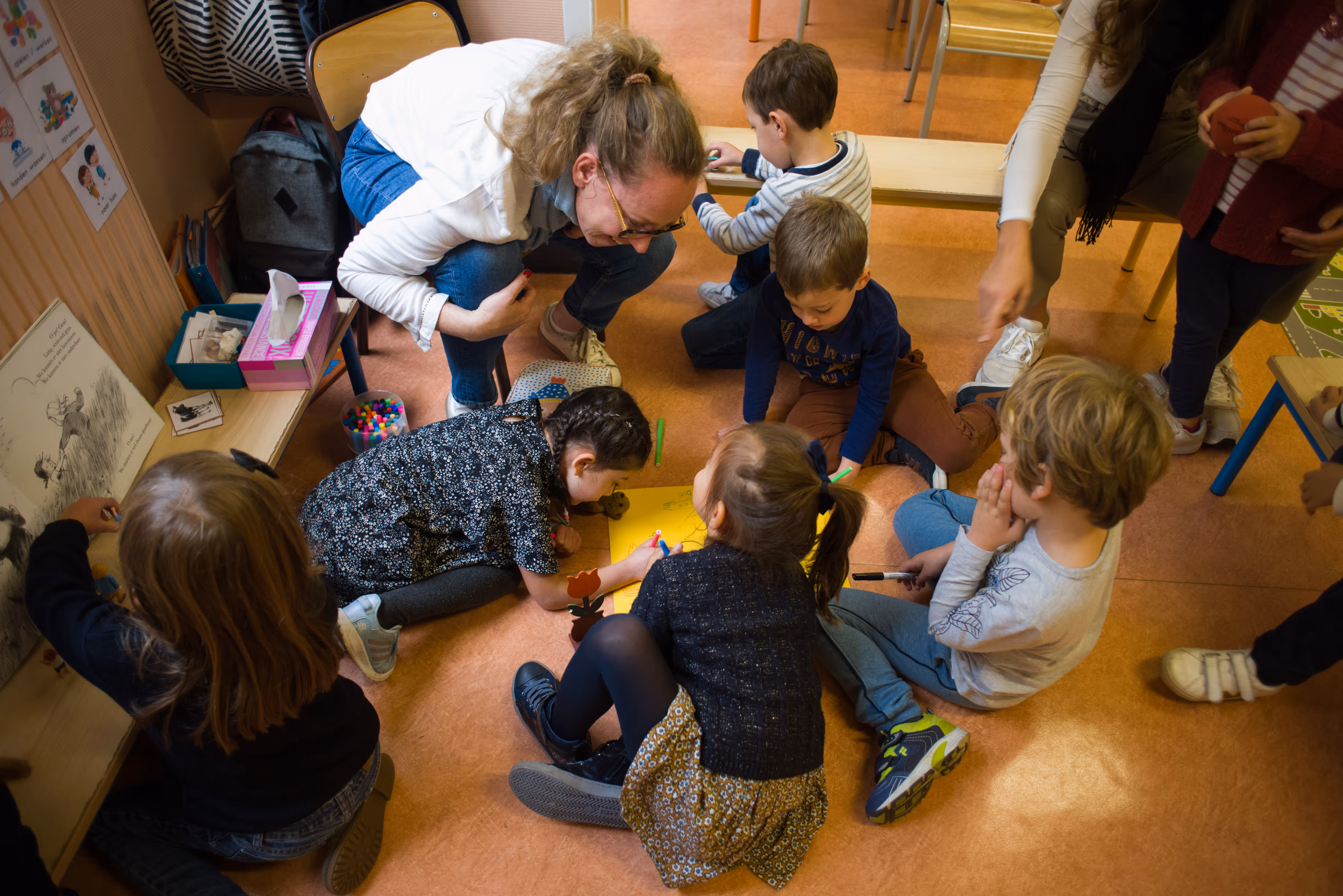 Leraar die met groep jonge kinderen op de vloer speelt en knutselt in een klaslokaal.