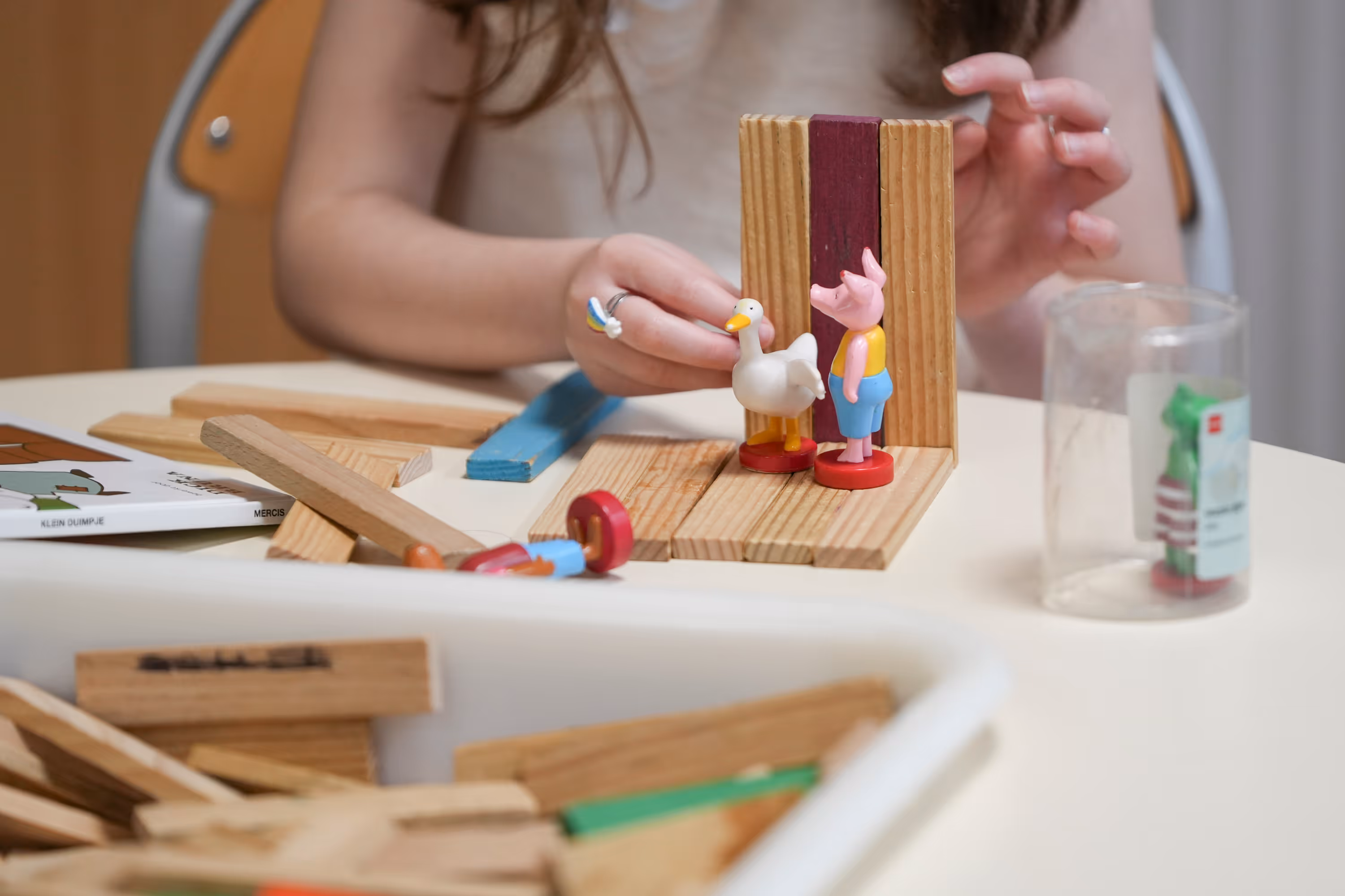 Kind speelt met houten blokken en houten dierfiguren aan een tafel.