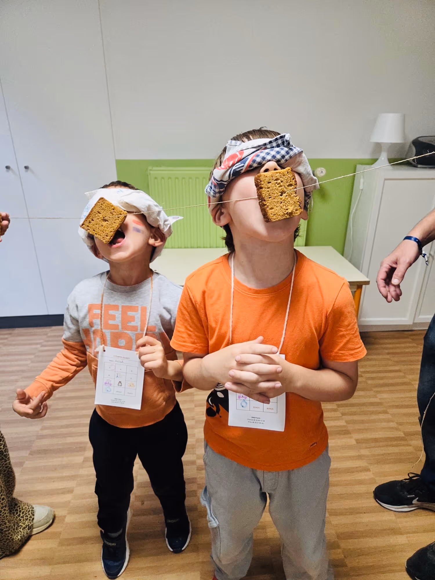 Twee blinde kinderen bijten in aan touw hangende vierkanten koekjes tijdens spel binnen.