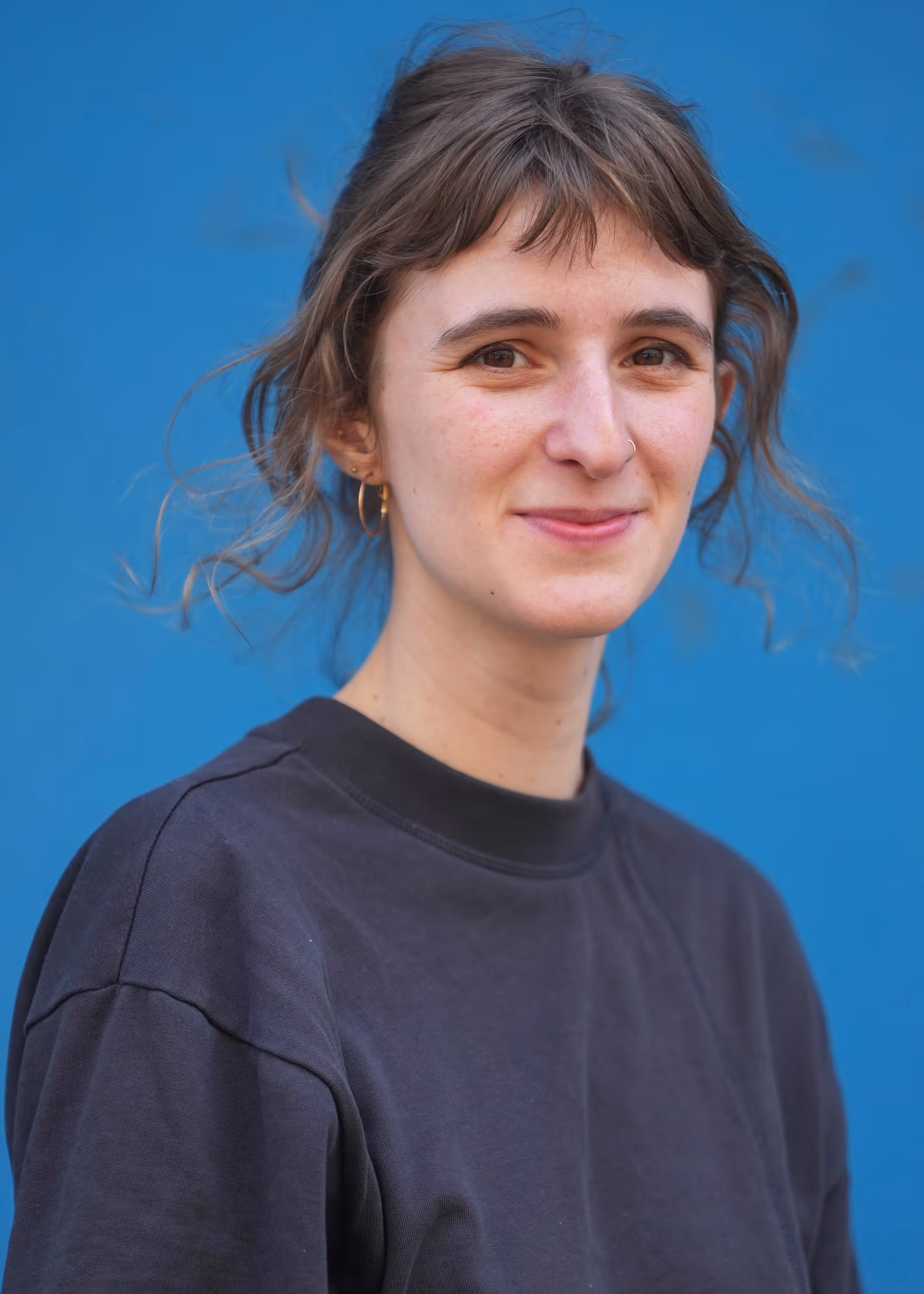 Vrouw met golvend haar en zwart shirt glimlacht voor een blauwe achtergrond.