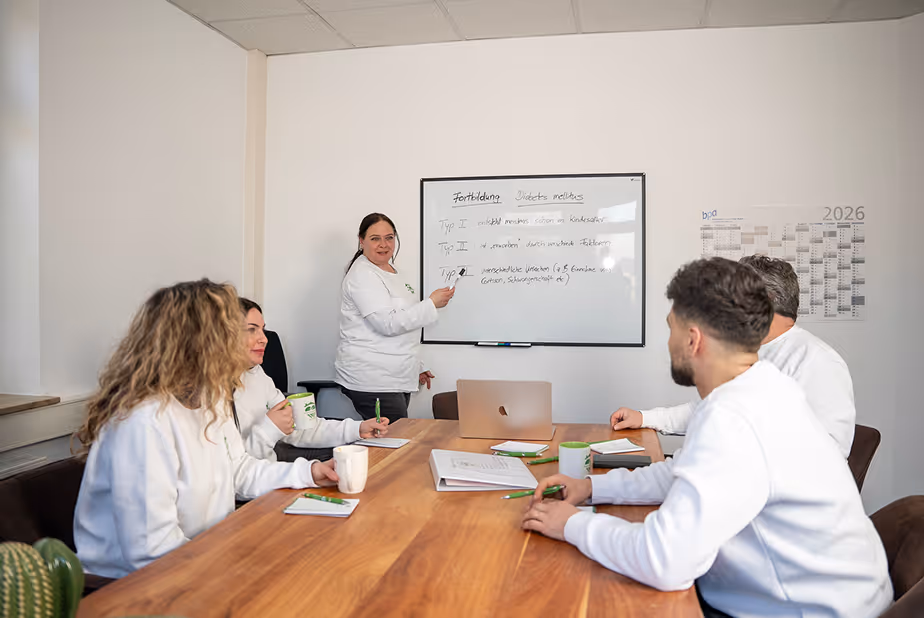 Das Team von Hand und Herz sitzt in einer Besprechung mit Laptop, Notizblöcken und Tassen an einem Holztisch.