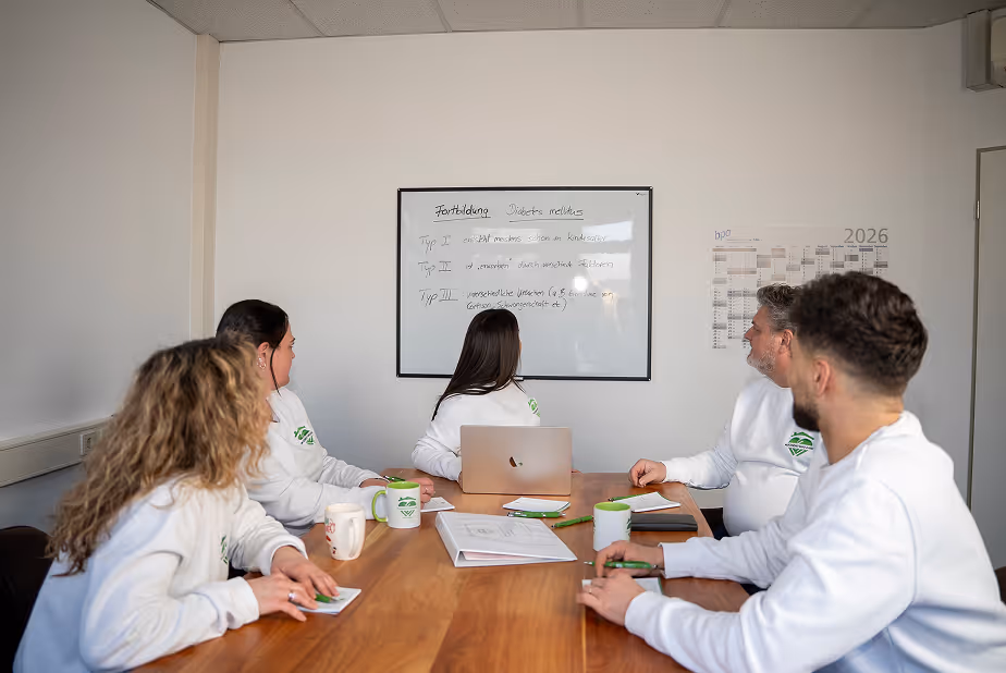 Das Team von Hand und Herz sitzt in einer Besprechung mit Laptop, Notizblöcken und Tassen an einem Holztisch.