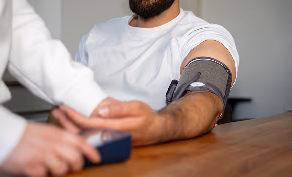 Ein Mann trägt eine Blutdruckmanschette am Oberarm, während eine Person seinen Puls misst.