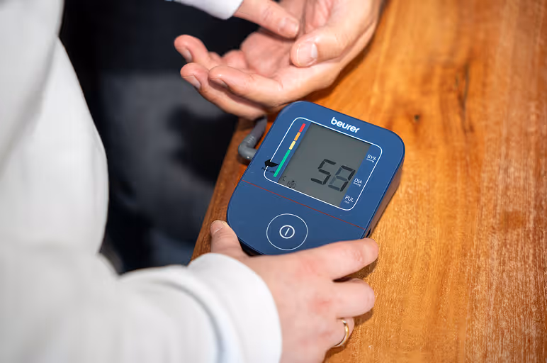 Person hält ein Beurer Blutdruckmessgerät mit einem Wert von 52 auf dem Display.