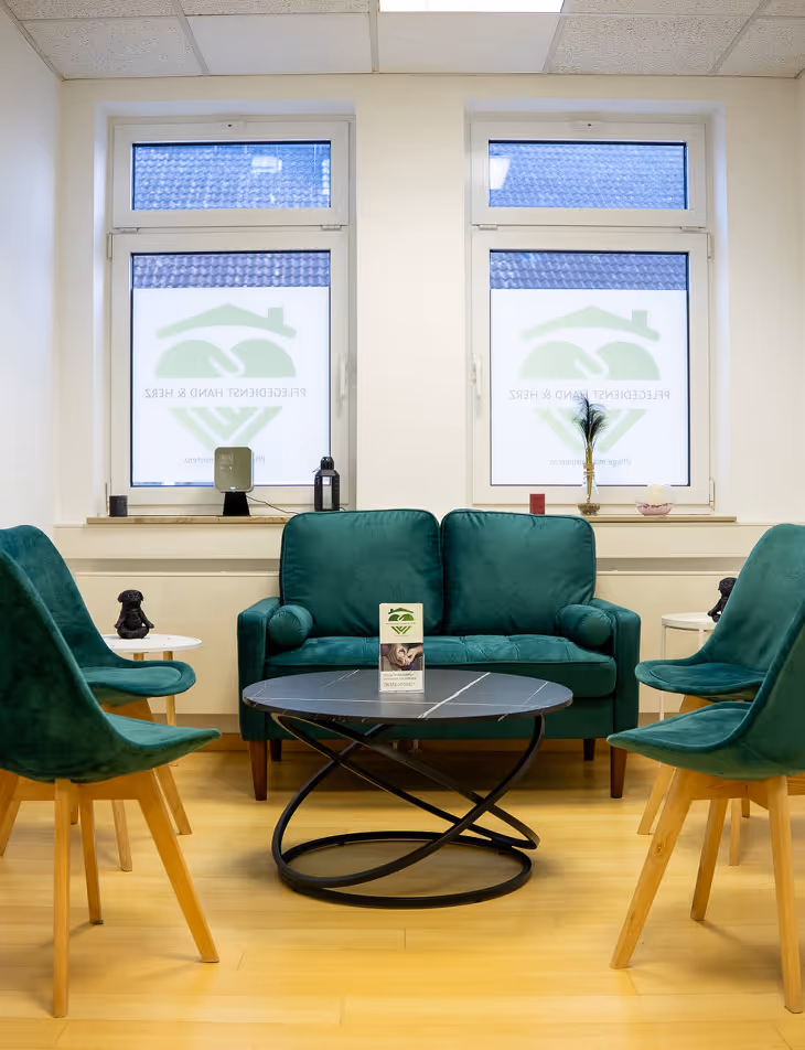 Gemütlicher Warteraum mit grünem Sofa, vier grünen Stühlen um einen modernen schwarzen Couchtisch, zwei Fenstern mit halbtransparenten Sichtschutzfolien.