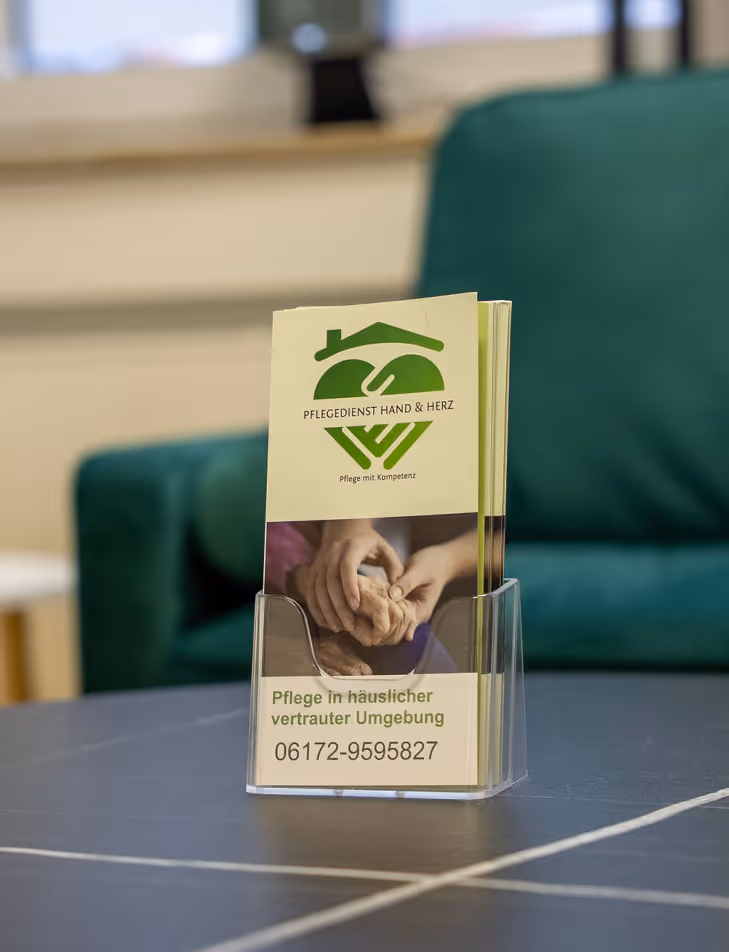 Flyer von Pflegedienst Hand & Herz mit grünem Logo, Foto von Handpflege und der Telefonnummer 06172-9595827 auf einem Tisch.