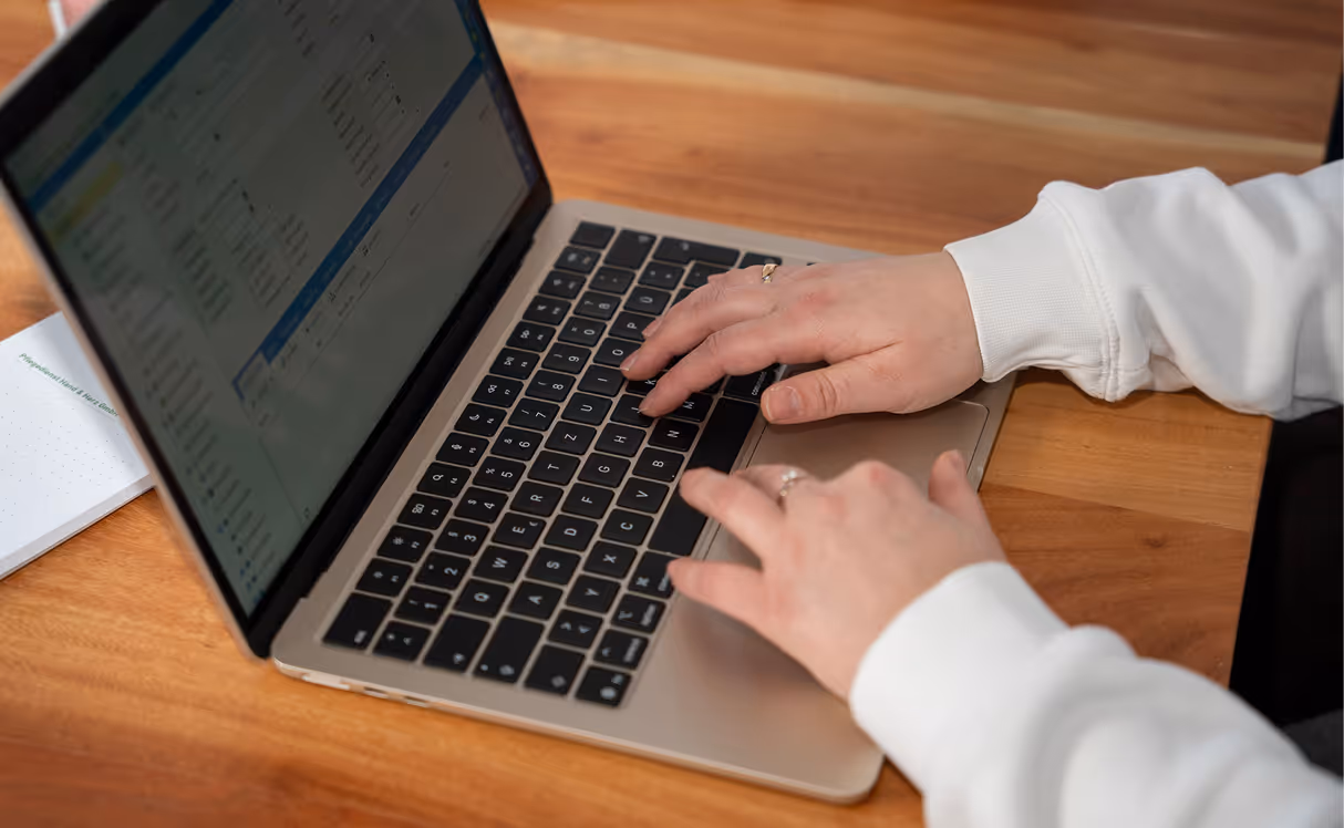 Person, die auf einem Laptop mit sichtbarem Bildschirm und Tastatur tippt, auf einem Holztisch.