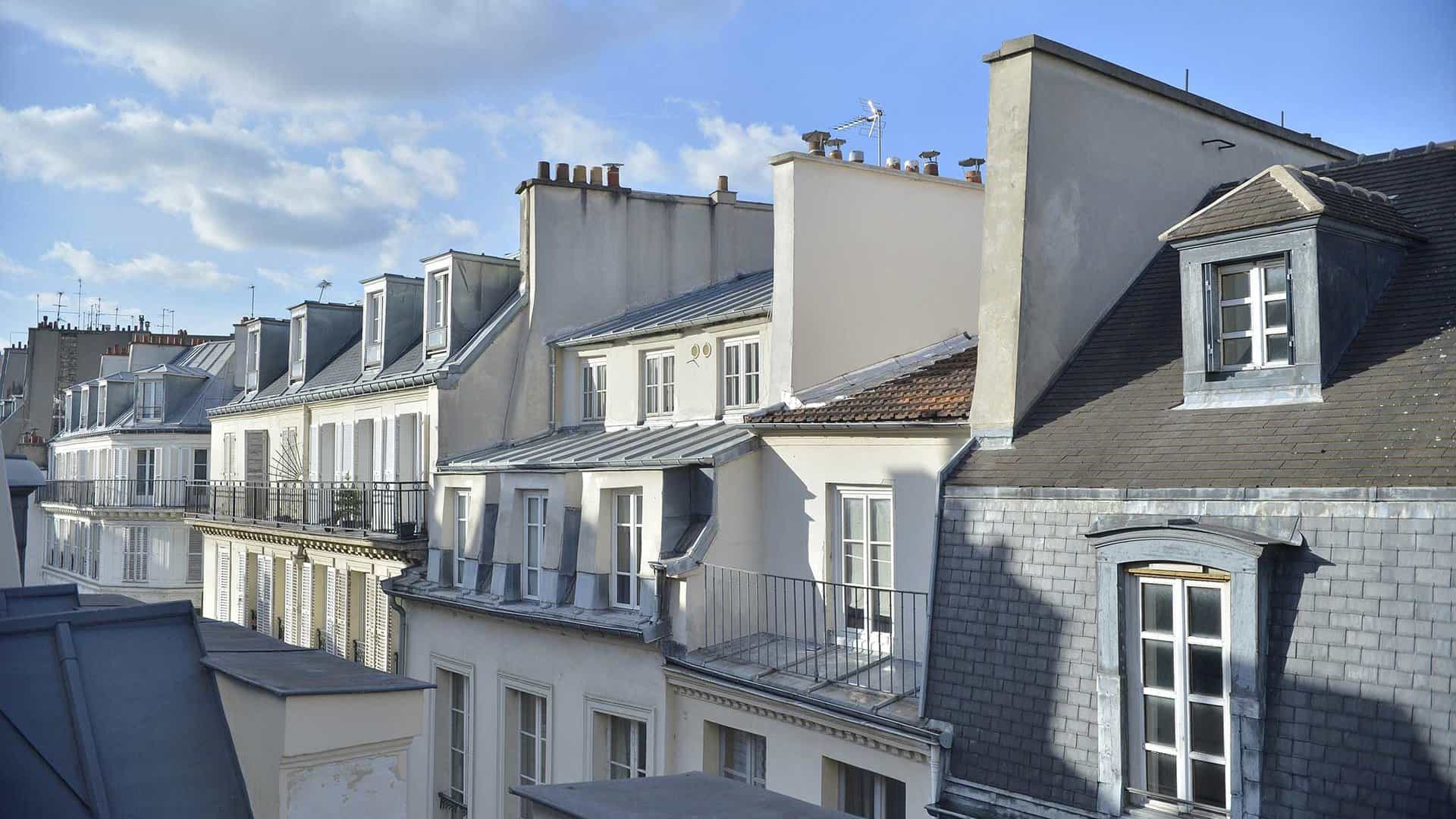 Façades d'immeubles haussmanniens et de l'hôtel Eugénie avec toits mansardés sous un ciel partiellement nuageux.