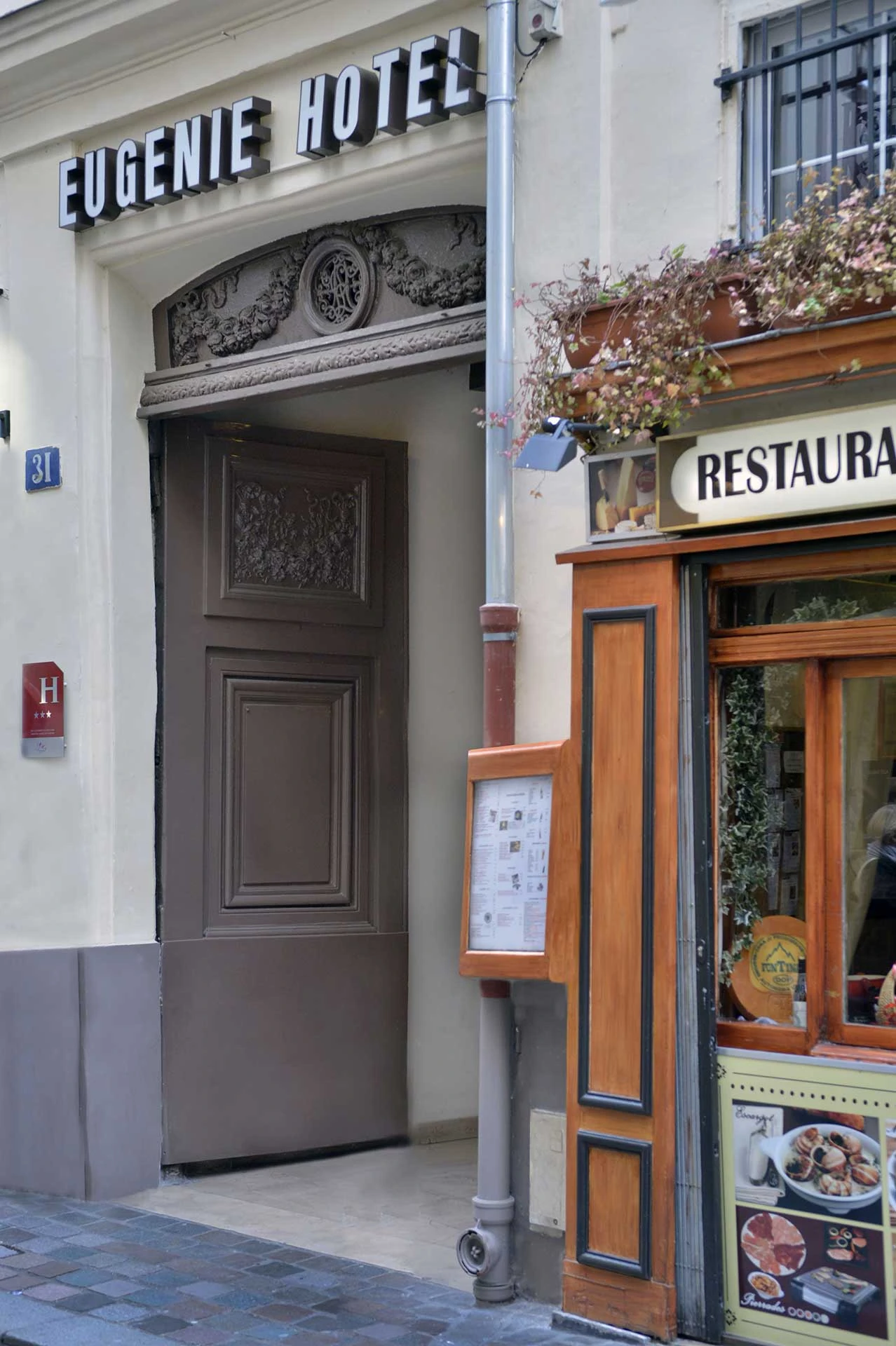 Façade de l'hôtel Eugenie avec une porte ouverte et un restaurant adjacent avec menu affiché.