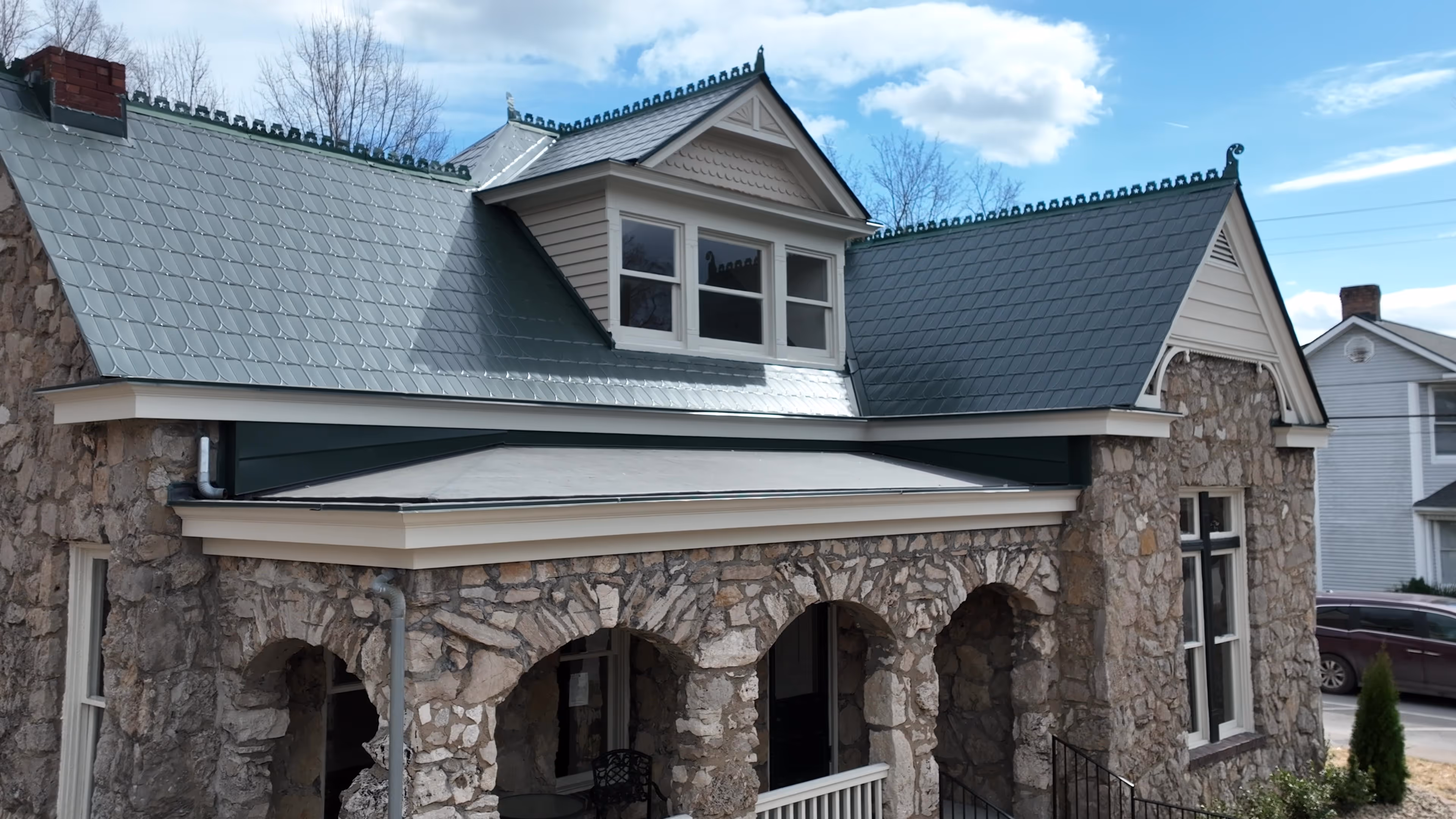 Stone house with green metal roof, arched porch, and three upper windows under blue sky.