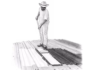 Man wearing a hat stands on a wooden deck holding a paint roller.