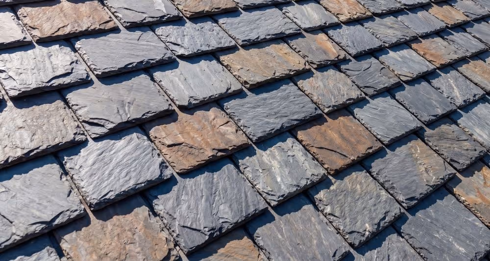 Close-up of a roof covered with overlapping rectangular slate tiles in gray and brown tones.