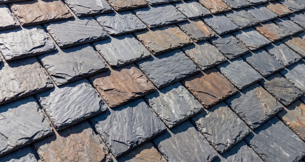 Close-up of a roof covered with overlapping rectangular slate tiles in gray and brown tones.