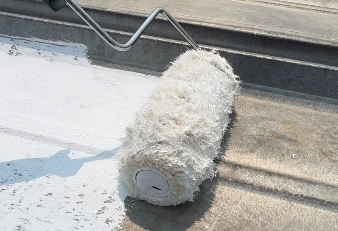 Paint roller applying white paint on a rough concrete surface outdoors.