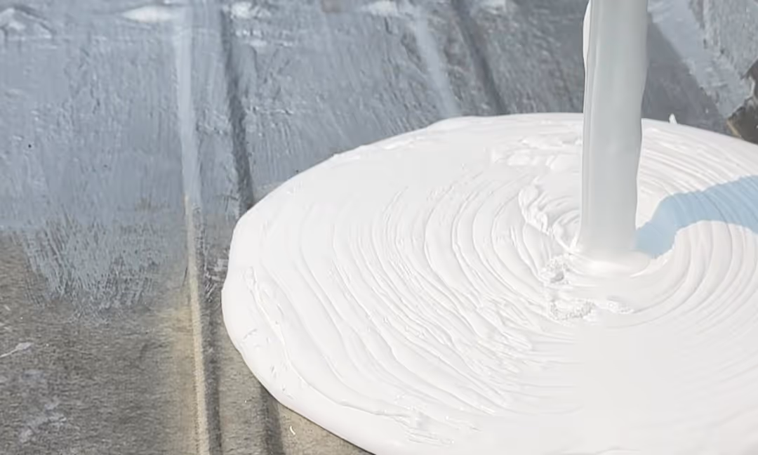 White paint being poured in a spiral motion on a gray surface.