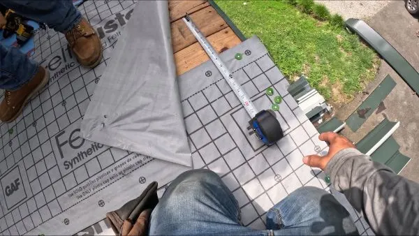 Person working on a roof with synthetic underlayment, measuring with a tape and metal ruler.