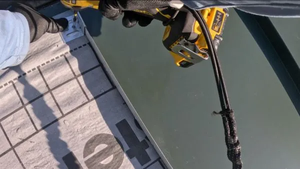 Worker wearing gloves securing metal standing seam roofing panels with a power tool.