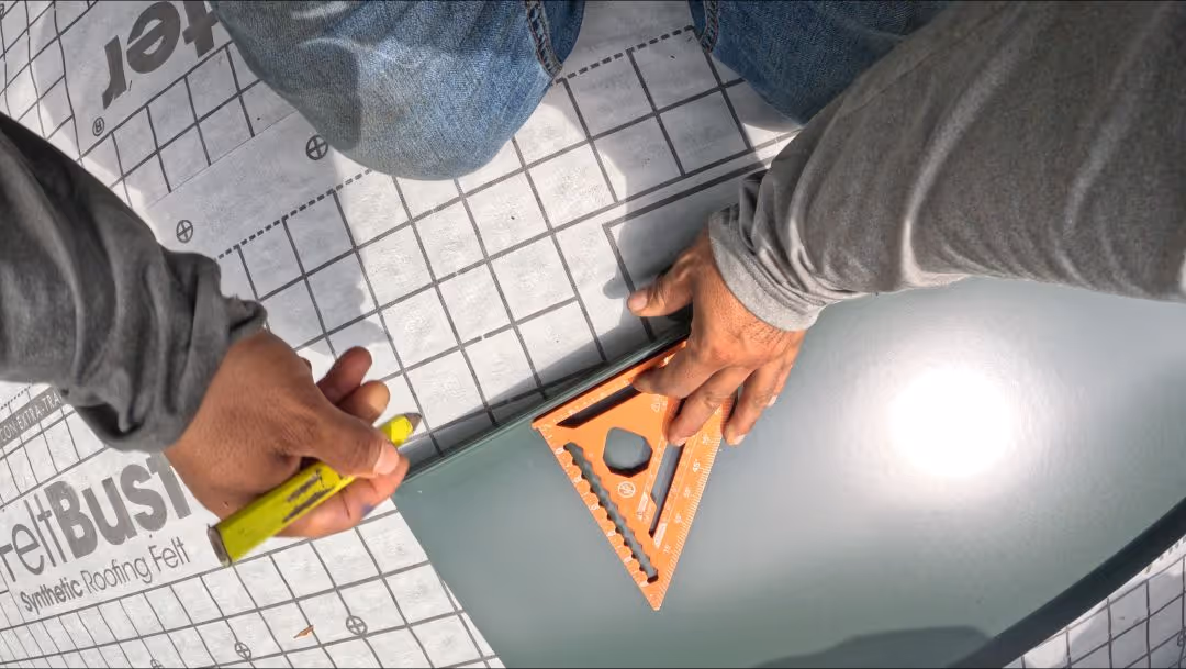 Person measuring and marking a standing seam metal panel with a square tool and yellow marker.