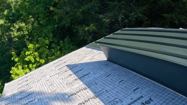 A rooftop with protective underlayment and a newly installed dark green standing seam metal panel.
