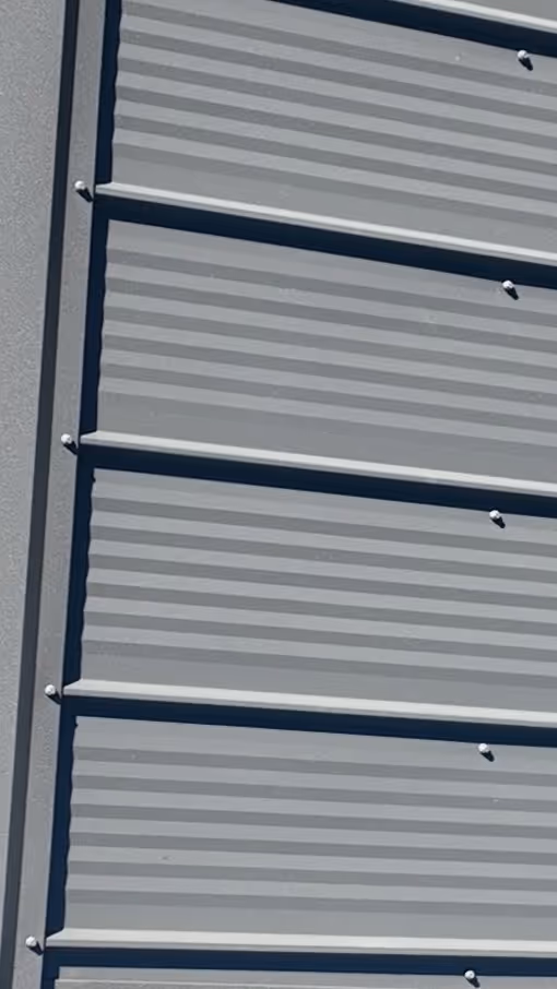 Close-up of gray metal siding panels with horizontal ridges and bolts on a building exterior.