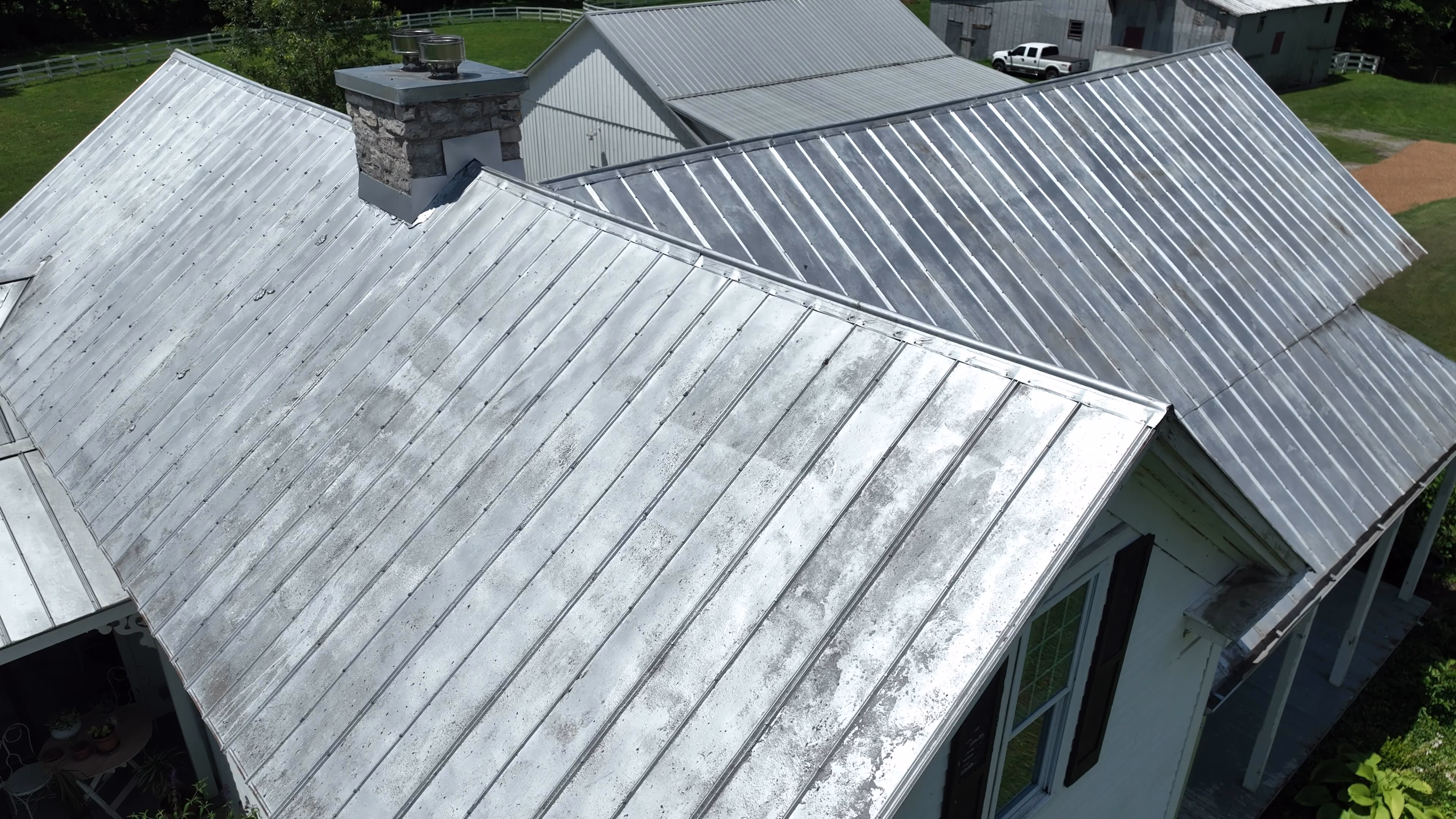 Aerial view of a house with large, weathered metal roofs and a stone chimney.