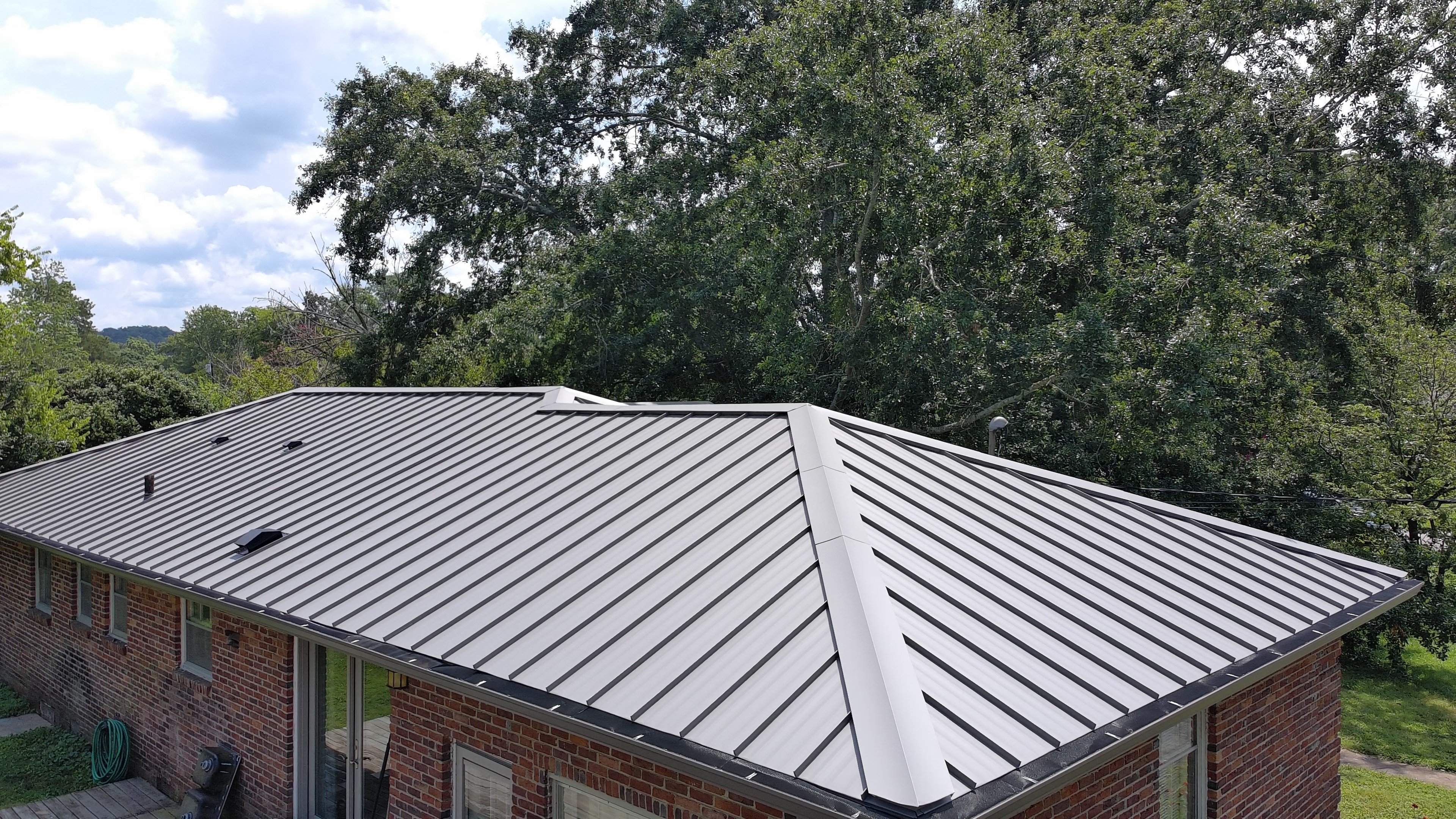 Aerial view of a silver standing seam metal hip roof on a brick ranch home at dusk in Franklin, Tennessee