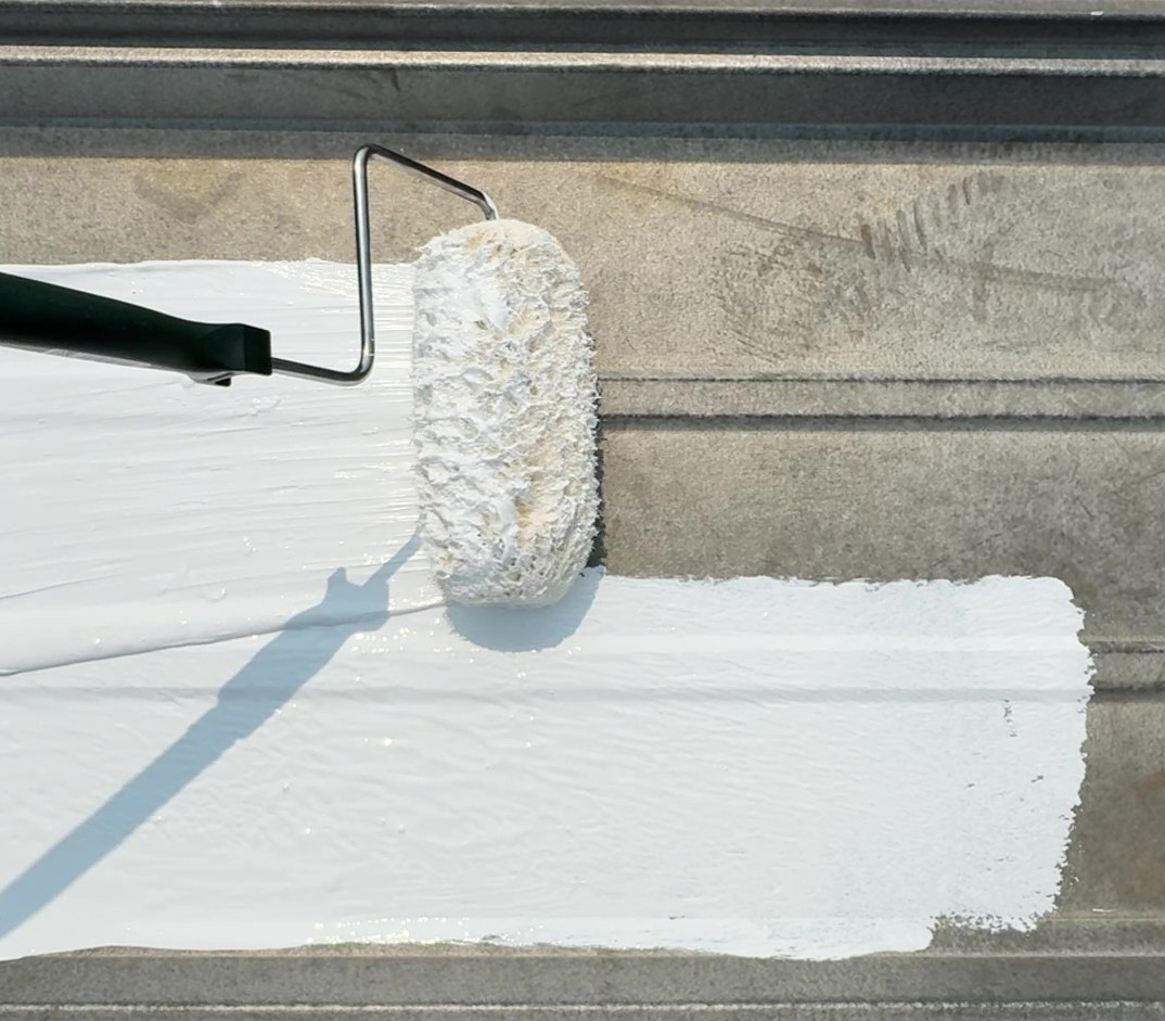 White silicone roof coating being rolled onto a metal roof