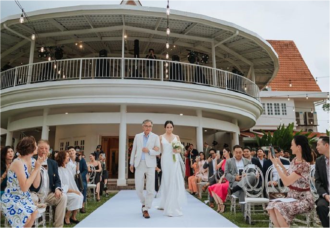 A bride walks down the aisle with her father at a garden wedding at Whitehouse @ The Estate, showcasing the personal and heartfelt atmosphere of an outdoor ceremony.