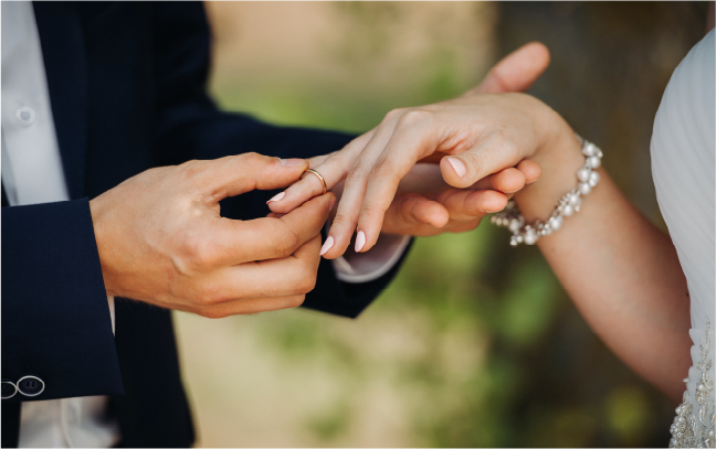 A close-up of a groom placing a wedding ring on his bride's finger, highlighting the intimate and deeply personal moments of a garden wedding.