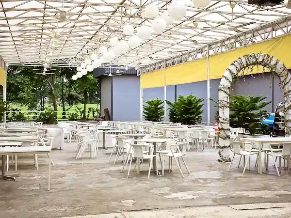 The airy, semi-outdoor event space at Glasshouse at Seputeh, with white tables and chairs set up for a corporate dinner or reception.