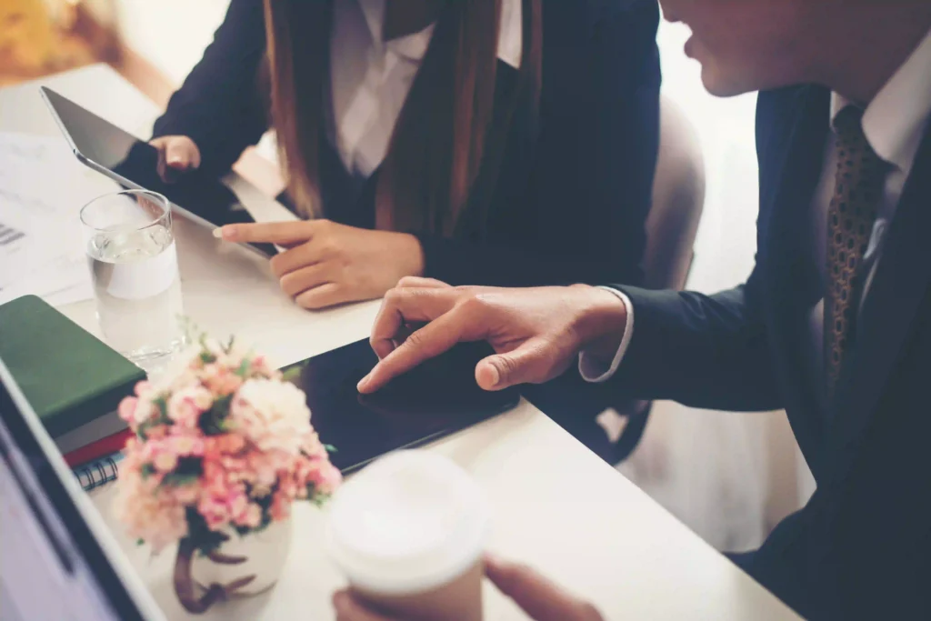 Two people at a desk review a digital tablet, their focused collaboration representing the importance of a team approach in wedding planning.