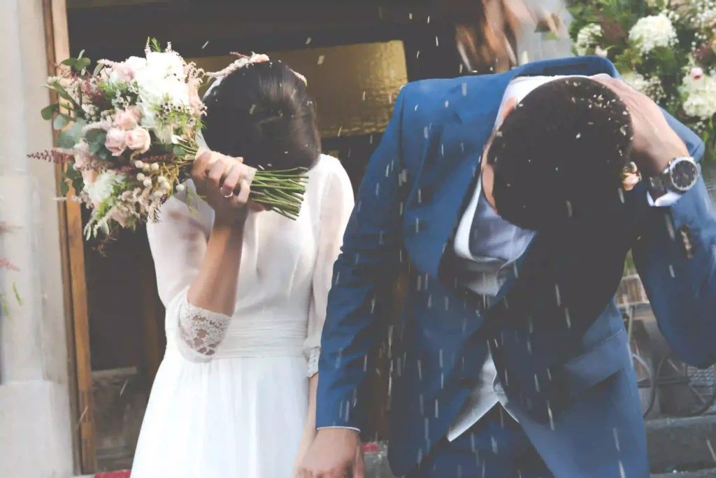 A wedding couple ducks under a shower of confetti or petals, a visual metaphor for how unexpected elements like rain are less of a problem than the uncertainty of not having a backup plan.