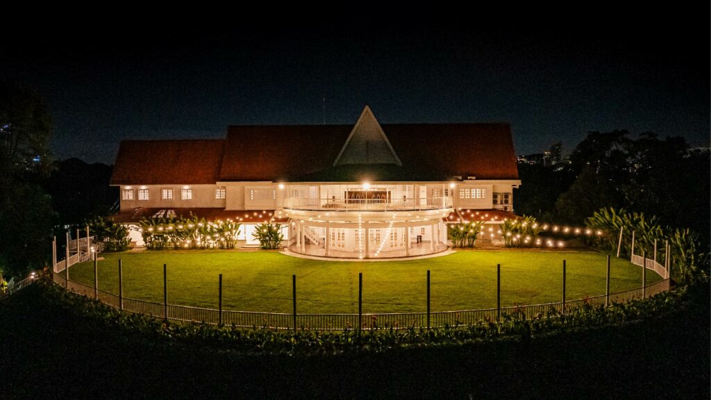 night photo of Whitehouse @ The Estate. The main building is brightly lit, with its pointed roof and circular balcony standing out against the night sky.