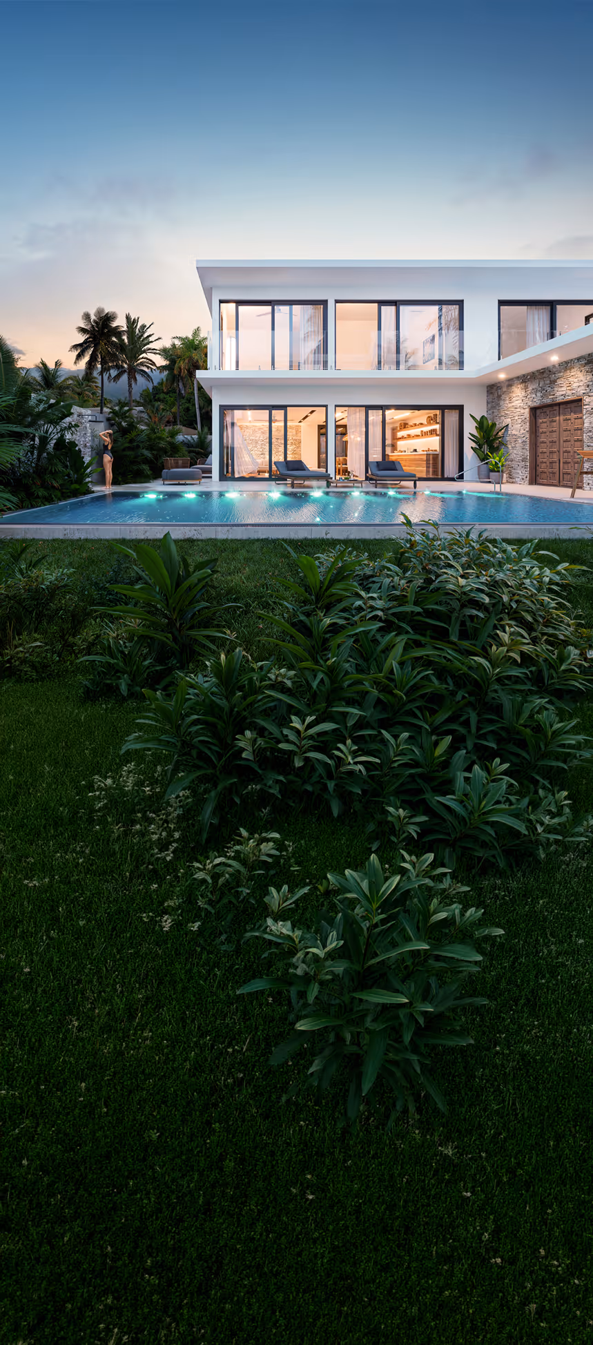 Modern two-story house with large glass windows, a lit swimming pool, and lush green plants at dusk.