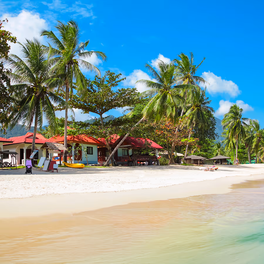 Tropical beach with white sand, palm trees, red-roofed bungalows, and a bright blue sky in Lamai, Koh Samui.