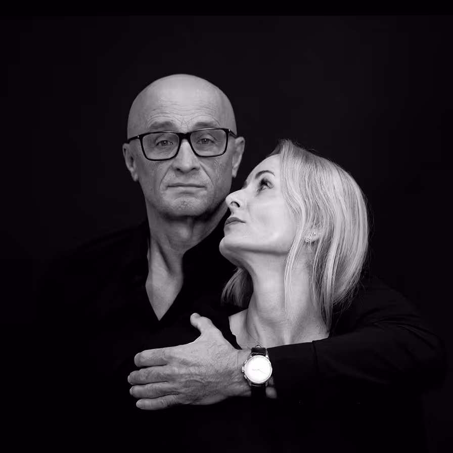 Black and white portrait of a man wearing glasses embracing a blonde woman who looks up at him.