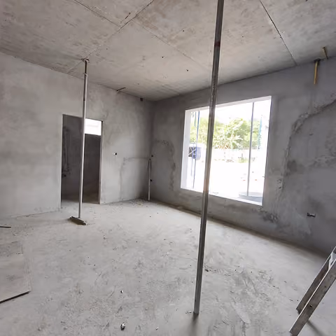 Unfinished room with concrete walls, two metal poles, and a large window showing greenery outside.