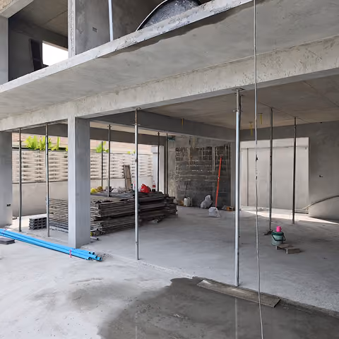 Concrete building under construction with metal support poles, stacked materials, and construction tools inside.