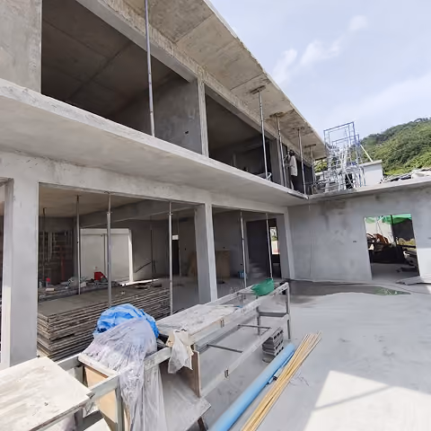 Partially constructed two-story concrete building with scaffolding and construction materials around.