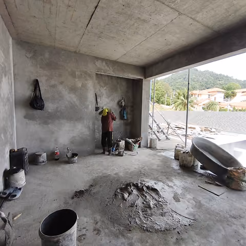 Construction worker plastering a concrete wall in an unfinished building with tools and materials around.
