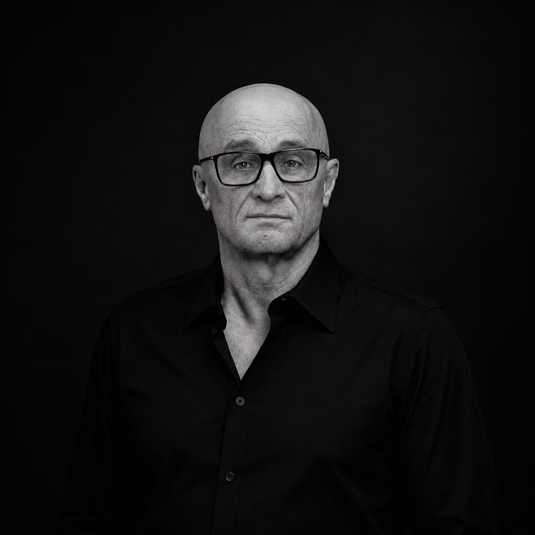 Karol Pajer with glasses wearing a black button-up shirt, looking straight ahead on a black background.