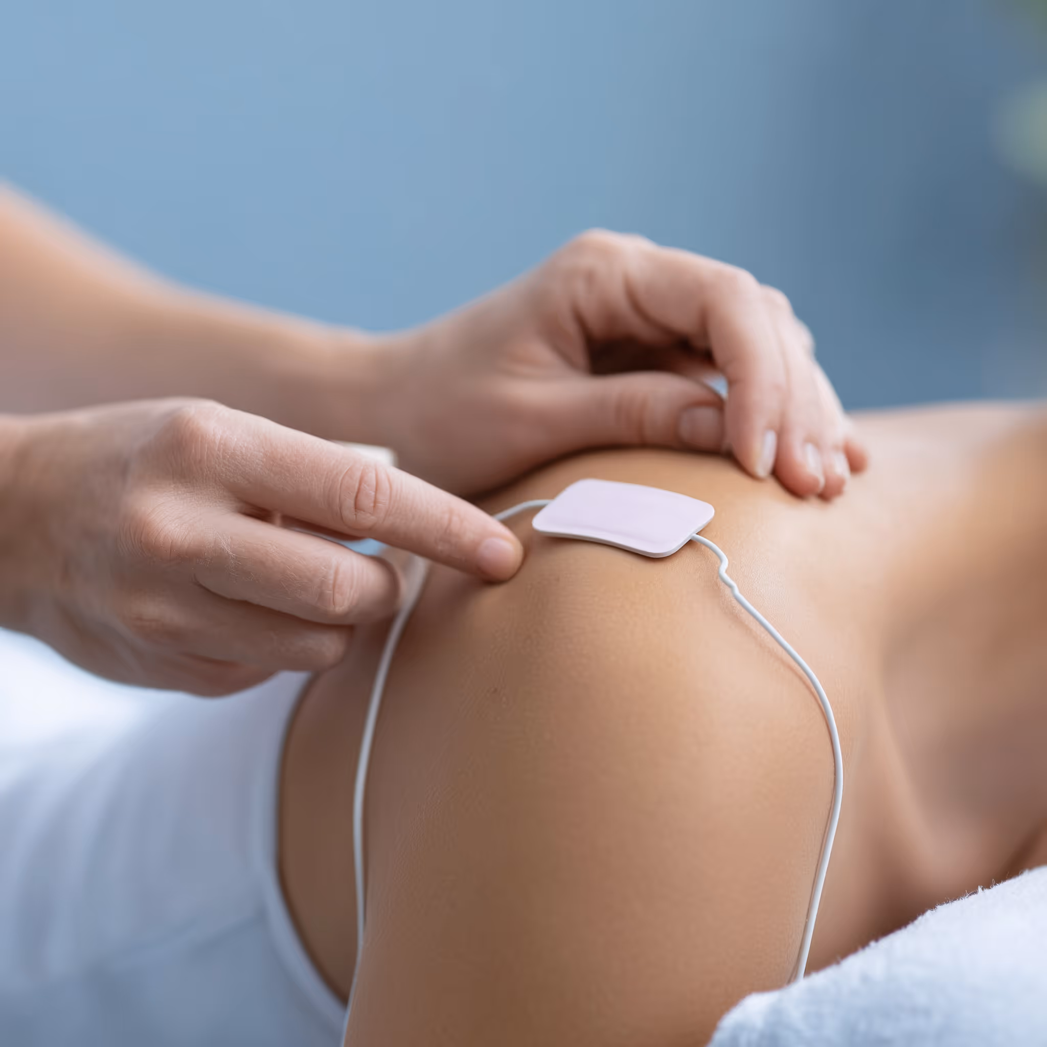 Eine Hand platziert ein Elektrodenpad zur Elektrotherapie auf einer Schulter.