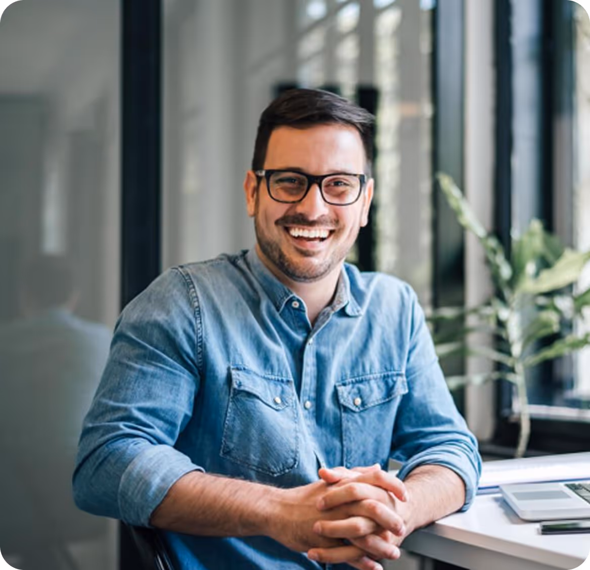 Un homme souriant portant des lunettes et une chemise en jean